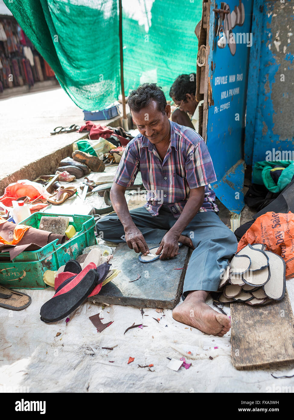 Two Indian men making shoes in a makeshift at the side of the