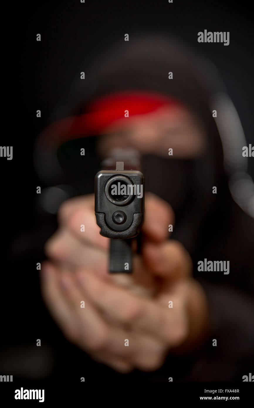 A young criminal points an automatic handgun at the viewer. Stock Photo
