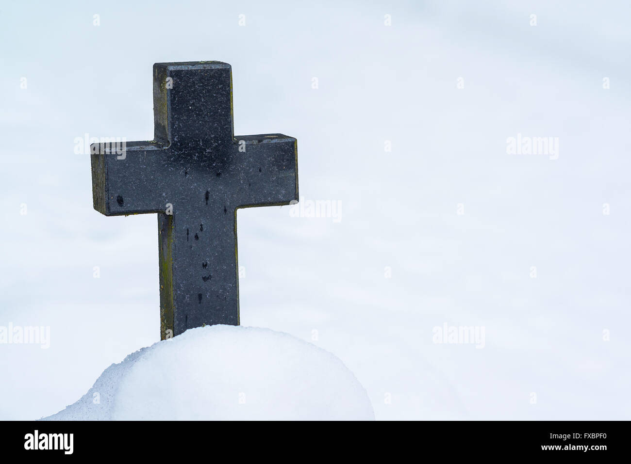 Closeup of black stone cross in cemetery and snow Stock Photo