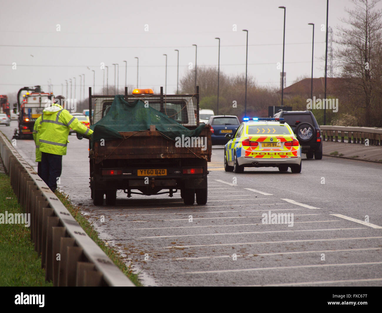 Newcastle Upon Tyne, UK. 14th April 2016. Stationary Northumbria police cars feeding traffic past a multi vehicle car crash on the 1058-coast road in North Tyneside earlier this morning as clean up crews make the carriage way save for motorists by removing debris and sanding any spillages from the vehicles involved in the accident. Credit:  james walsh/Alamy Live News Stock Photo