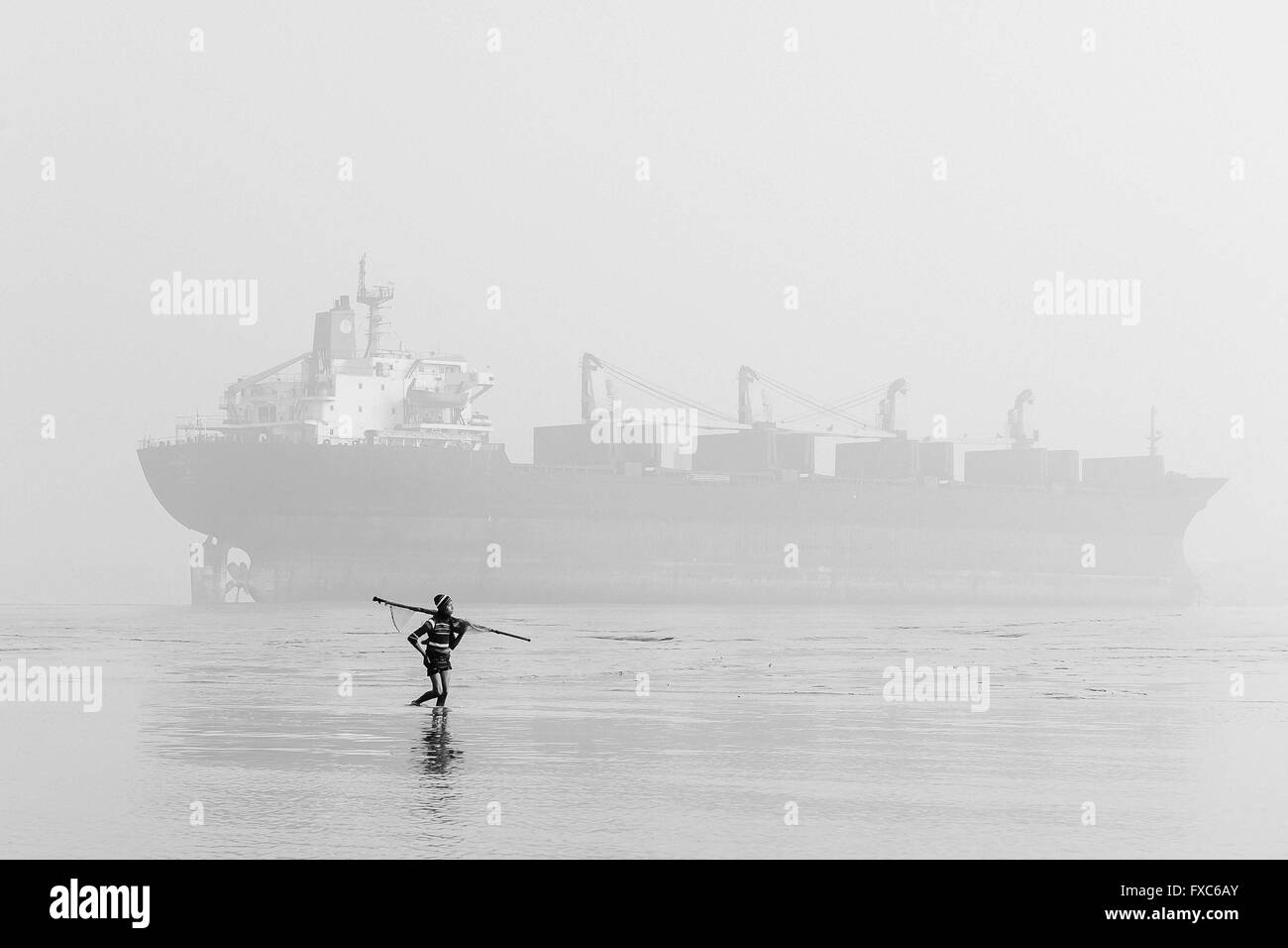 A boy goes with a hand net at dawn between the shipbreaking places of Chittagong in Bangladesh for fishing. Every morning, fishermen in Chittagong go with their boats to contaminated fishing spots in the middle of one of the largest shipbreaking places in the world. Stock Photo