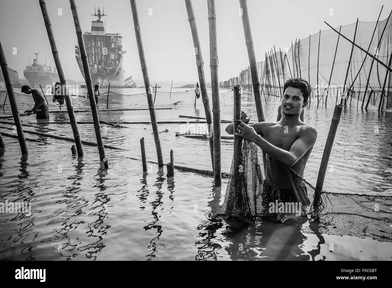 Fishermen between the shipbreaking places from Chittagong in Bangladesh are repairing their nets. Every morning fishermen in Chittagong go with their boats to contaminated fishing spots in the middle of one of the largest shipbreaking places the world. Stock Photo
