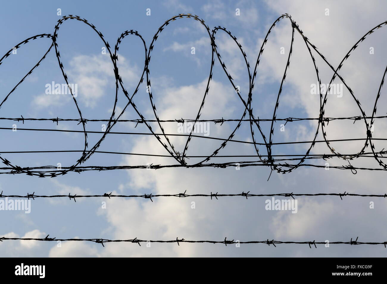 Prison wall barbed wire fence detail with blue sky in background Stock