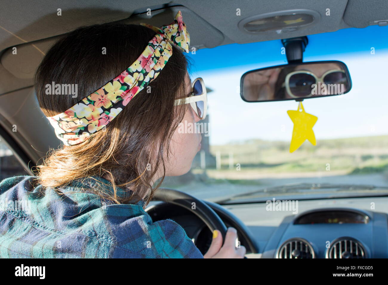 Young woman driving a car and looking herself at the mirror Stock Photo