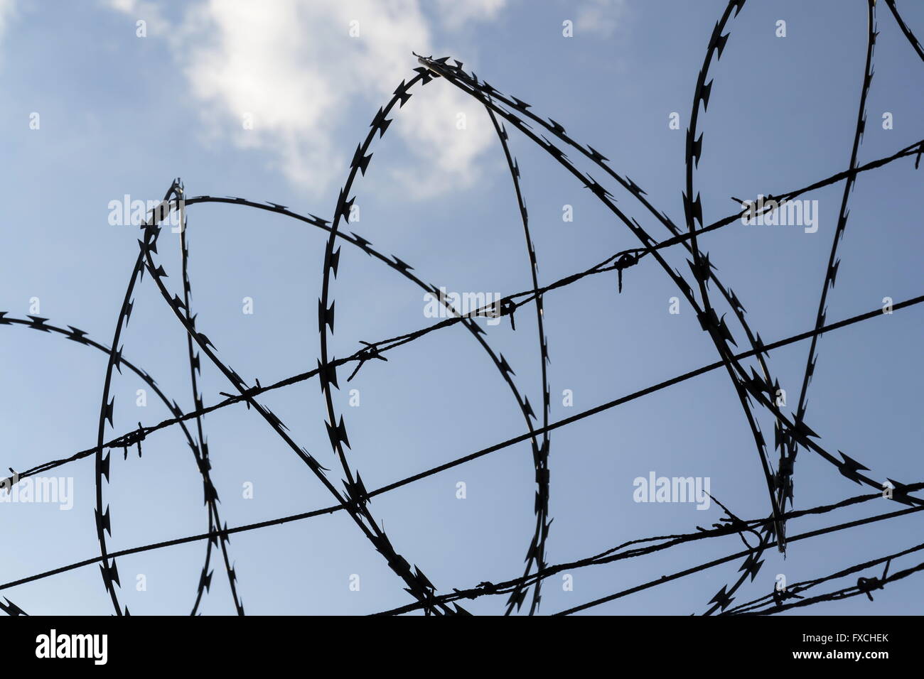 Prison wall barbed wire fence detail with blue sky in background Stock