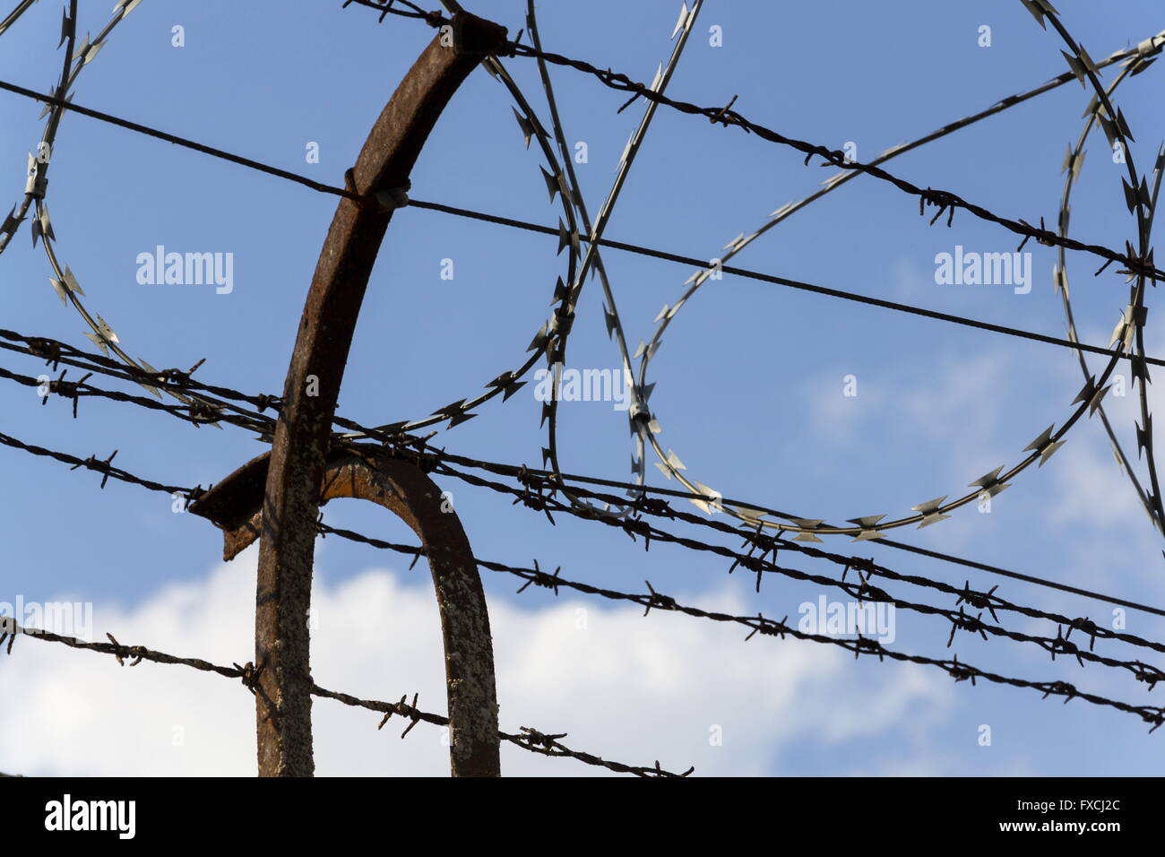 Prison wall barbed wire fence detail with blue sky in background Stock