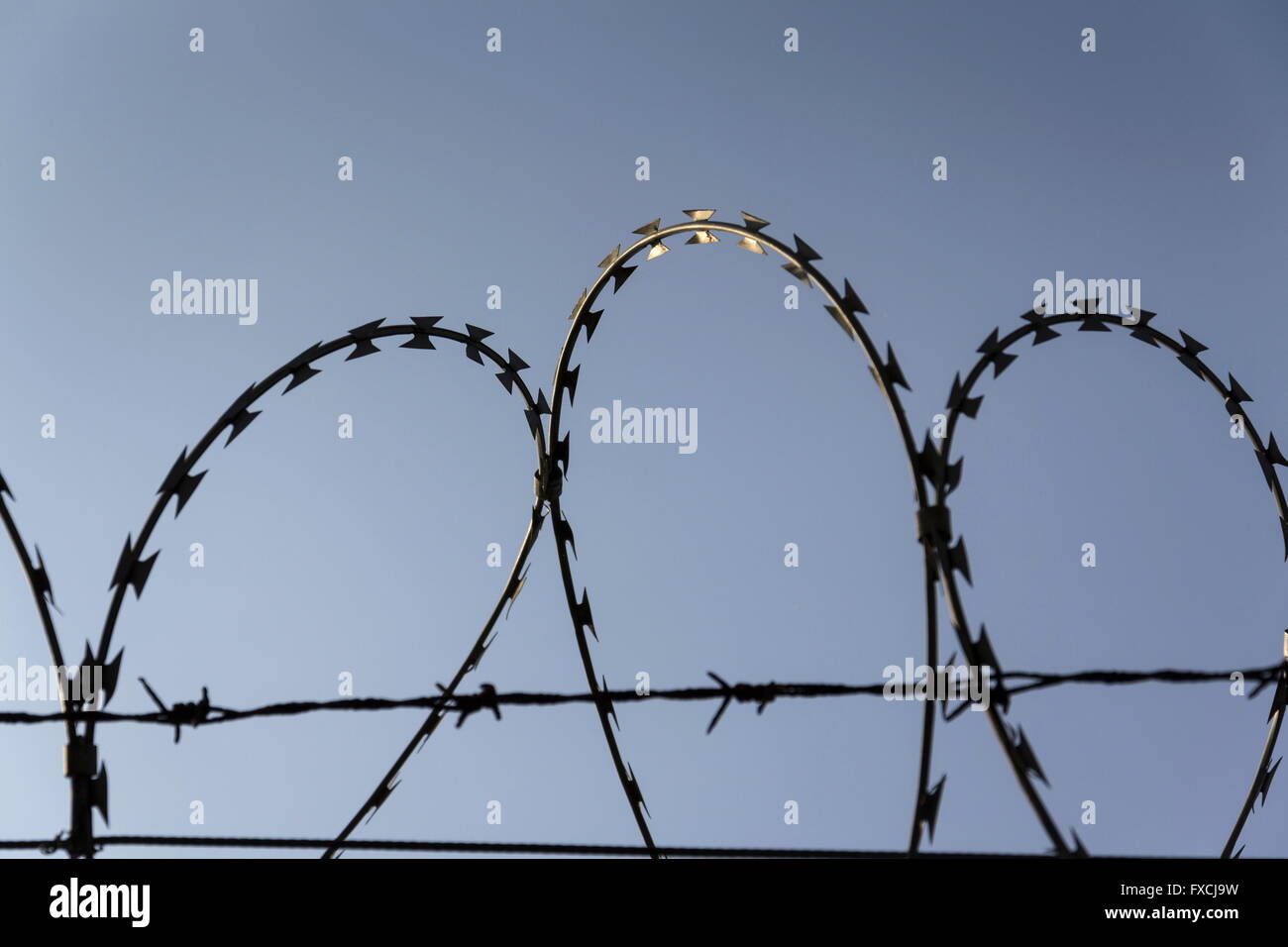 Prison wall barbed wire fence detail with blue sky in background Stock