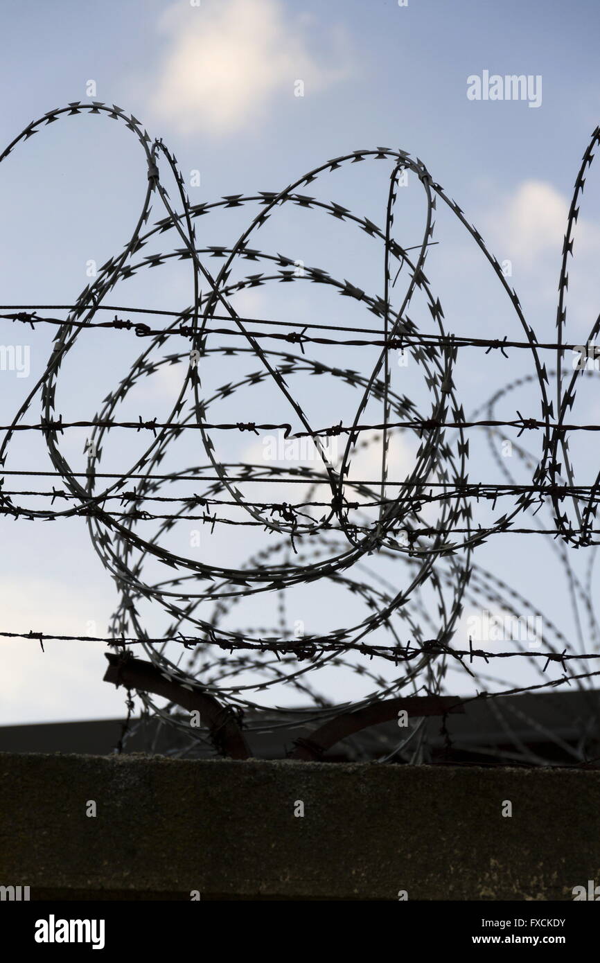 Prison wall barbed wire fence detail with blue sky in background Stock