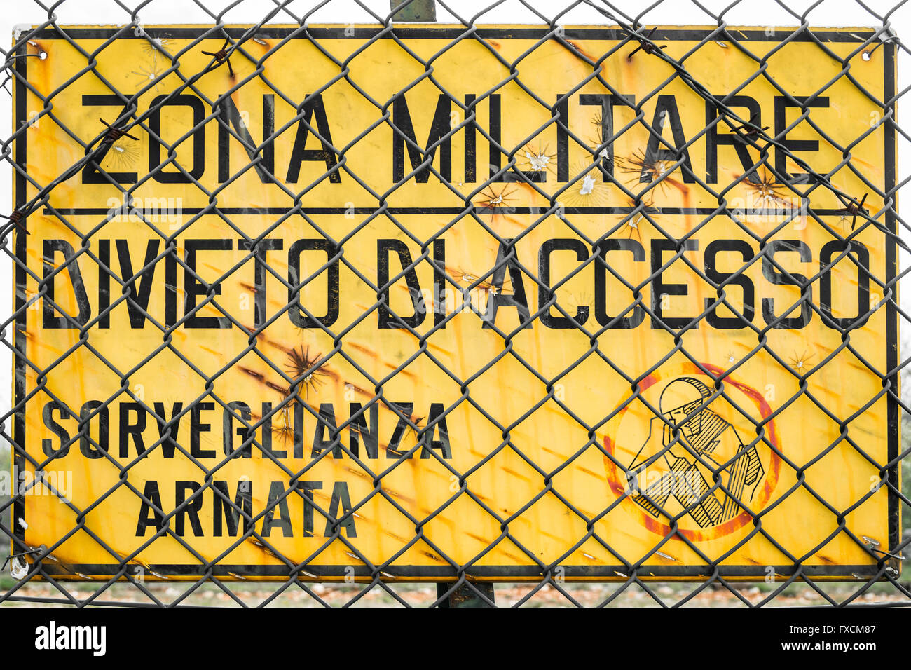 Yellow sign that reads in Italian 'military zone, no entry, armed surveillance'. Stock Photo