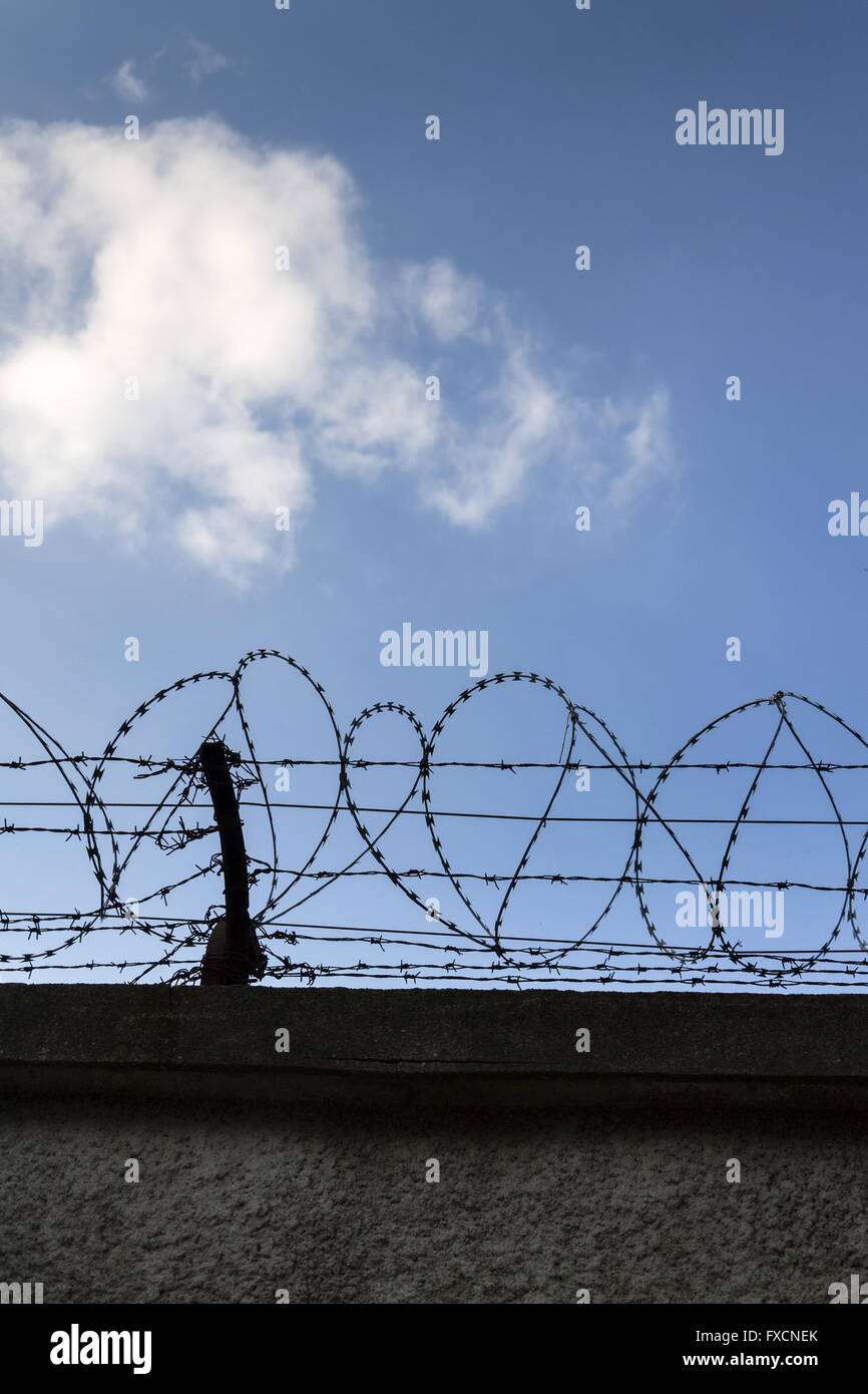 Prison wall barbed wire fence detail with blue sky in background Stock