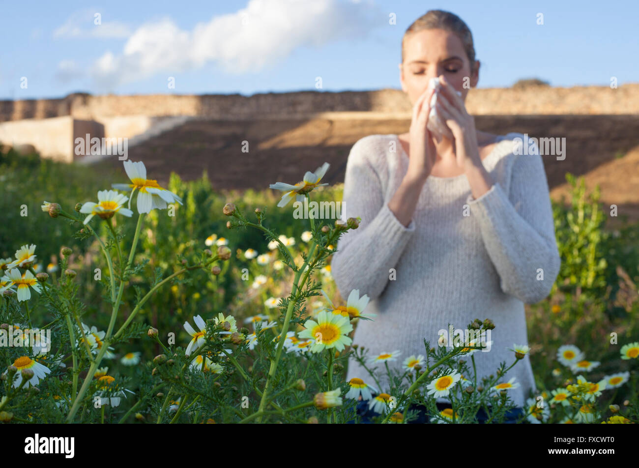Young woman sneezing in a daisy flowers meadow. She is allergic to