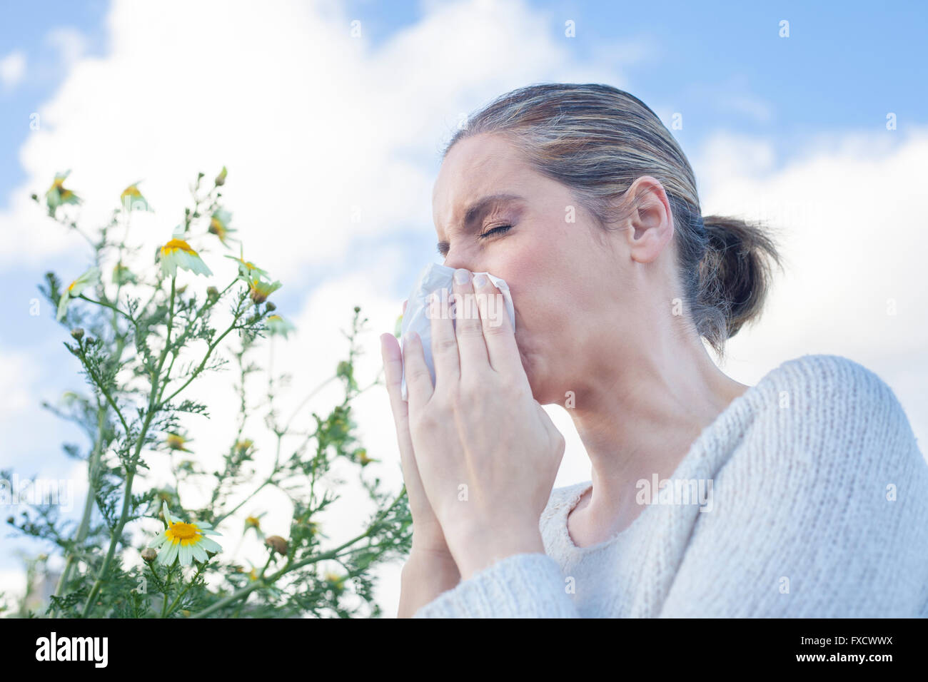 Young woman sneezing in a daisy flowers meadow. She is allergic to