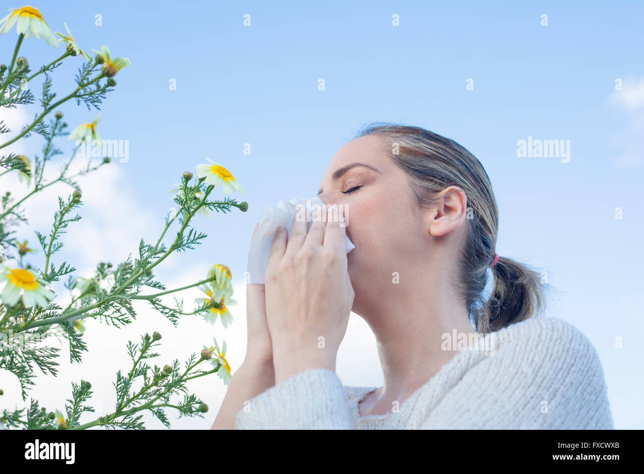 Young woman sneezing in a daisy flowers meadow. She is allergic to