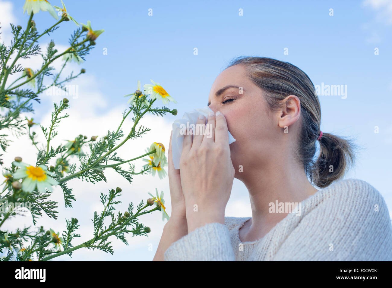 Young woman sneezing in a daisy flowers meadow. She is allergic to