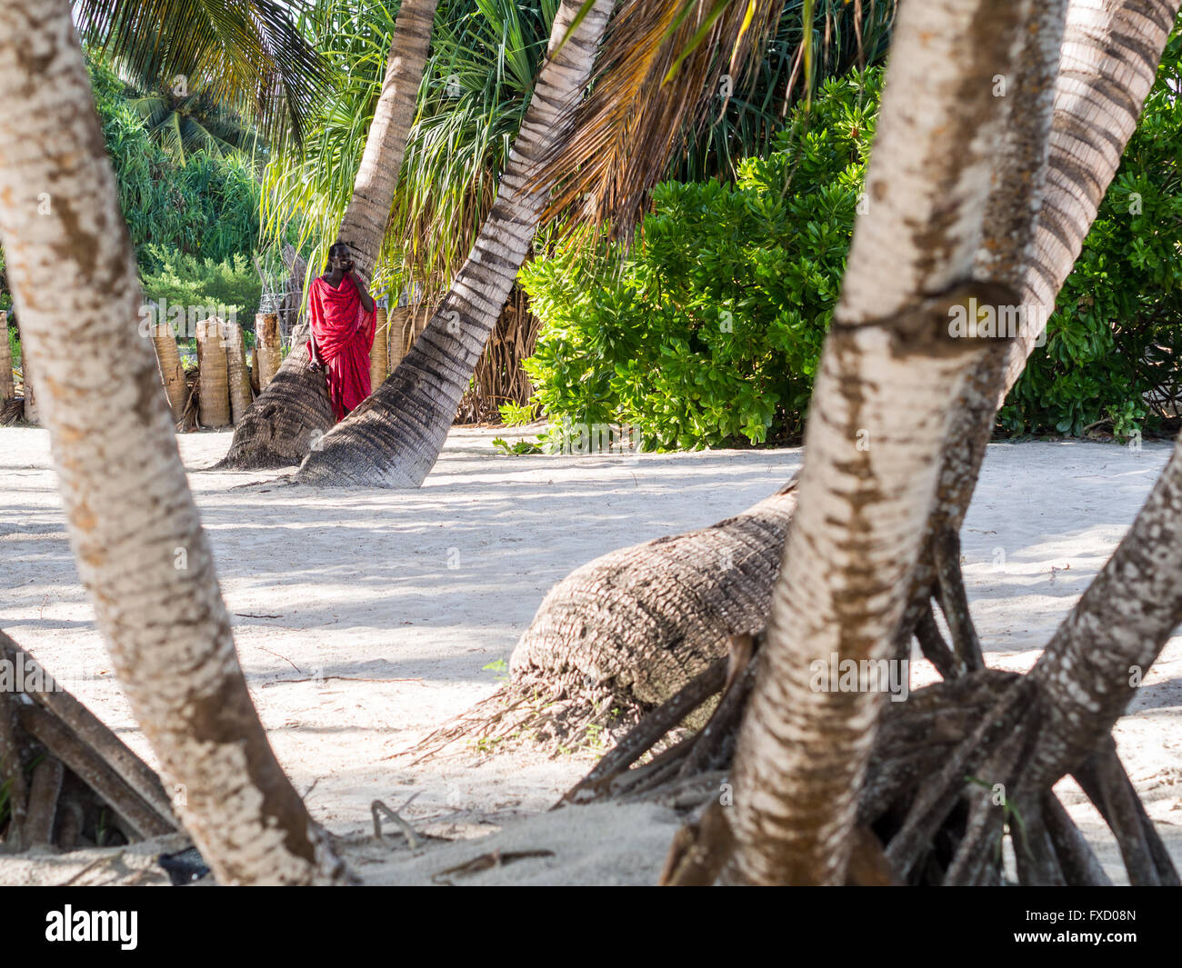 Masai warrior working as a security guard for one of the resorts talks on the phone on a beach. Stock Photo