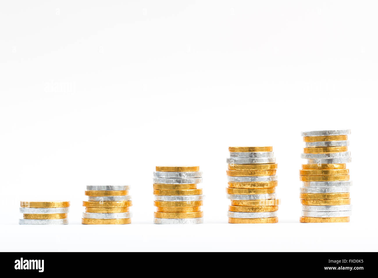 Columns and rows of gold and silver coins in the shape of an upward growth graph and on an isolated white background. Stock Photo