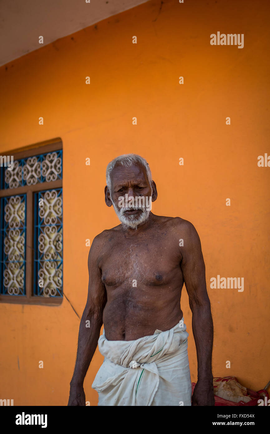 Old Indian man with beard and topless standing in front of his orange house in Kuilapalayam