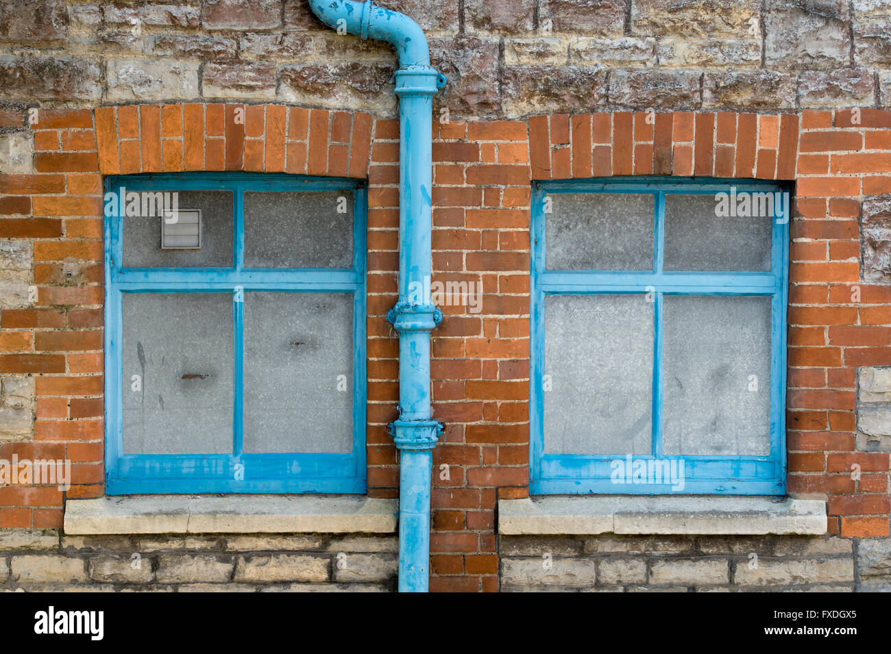 Stone and brick house wall with blue windows and drainpipe abstract. Glastonbury, Somerset, England Stock Photo