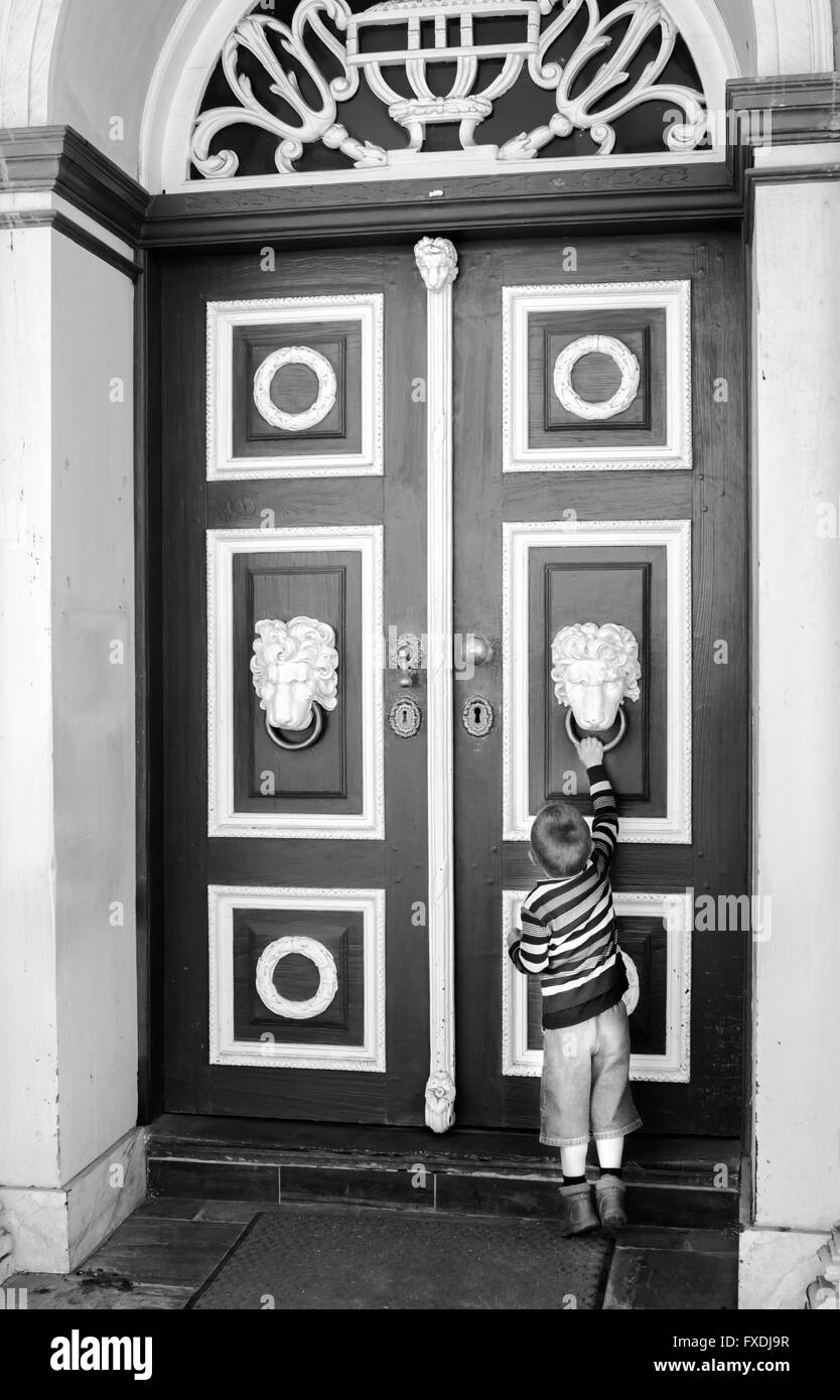 Little boy using brass knocker on big double door Stock Photo