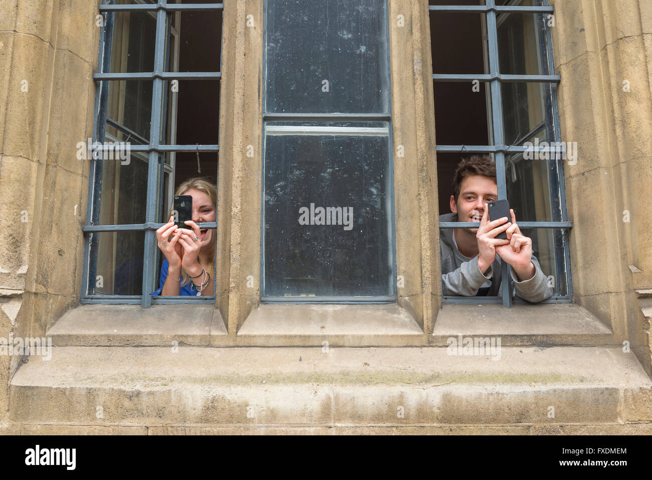 Couple taking photo, view of two Cambridge university students in Trinity College taking photos from an upstairs window, Cambridge, UK Stock Photo