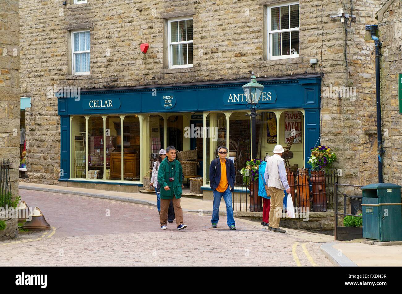 Chinese tourists walking past antiques shop in the Main Street. Hawes, Wensleydale, Yorkshire Dales National Park, Yorkshire, UK Stock Photo