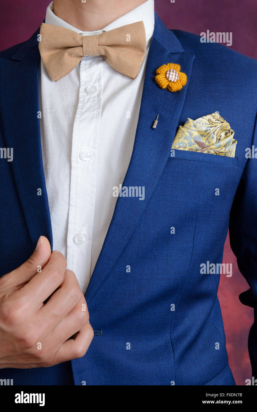 Man in blue suit with brown bow tie flower brooch and classic