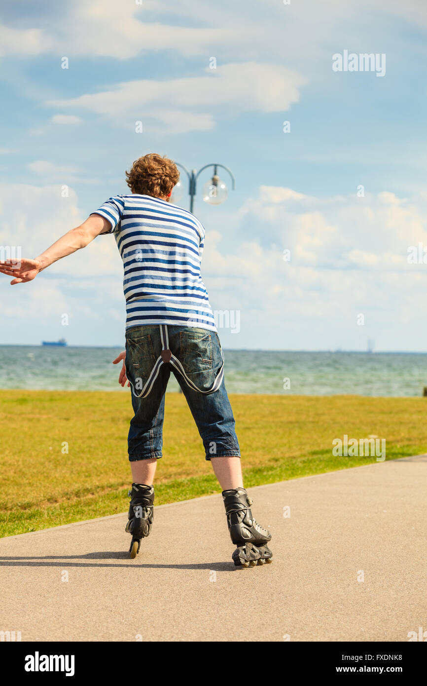 Holidays, active lifestyle freedom concept. Young fit man on roller skates riding outdoors on sea coast, guy rollerblading on sunny day Stock Photo