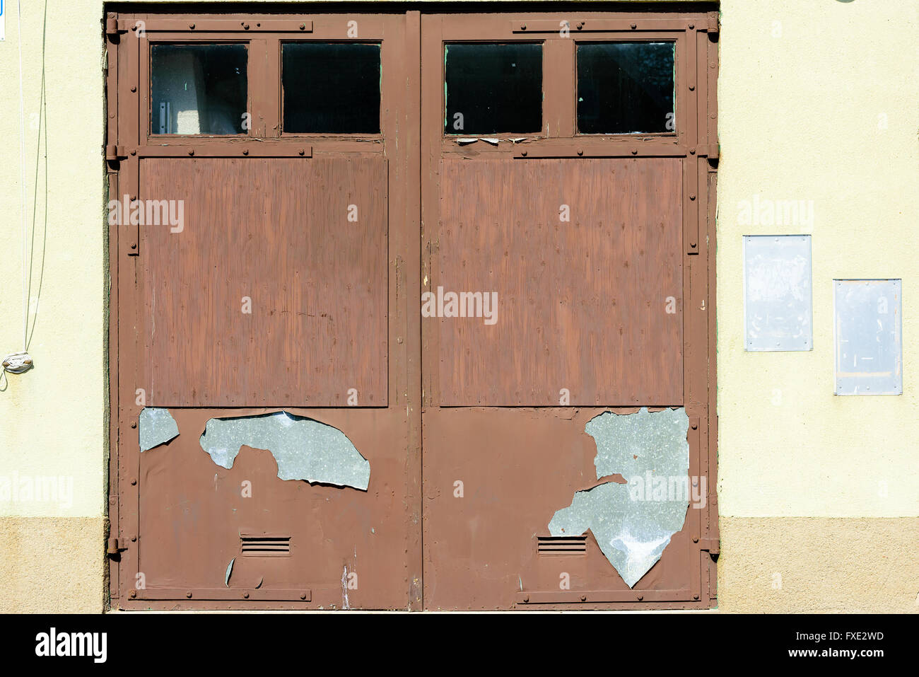 Brown garage door with flaking paint and weathered appearance. Empty signboards beside the door. Stock Photo