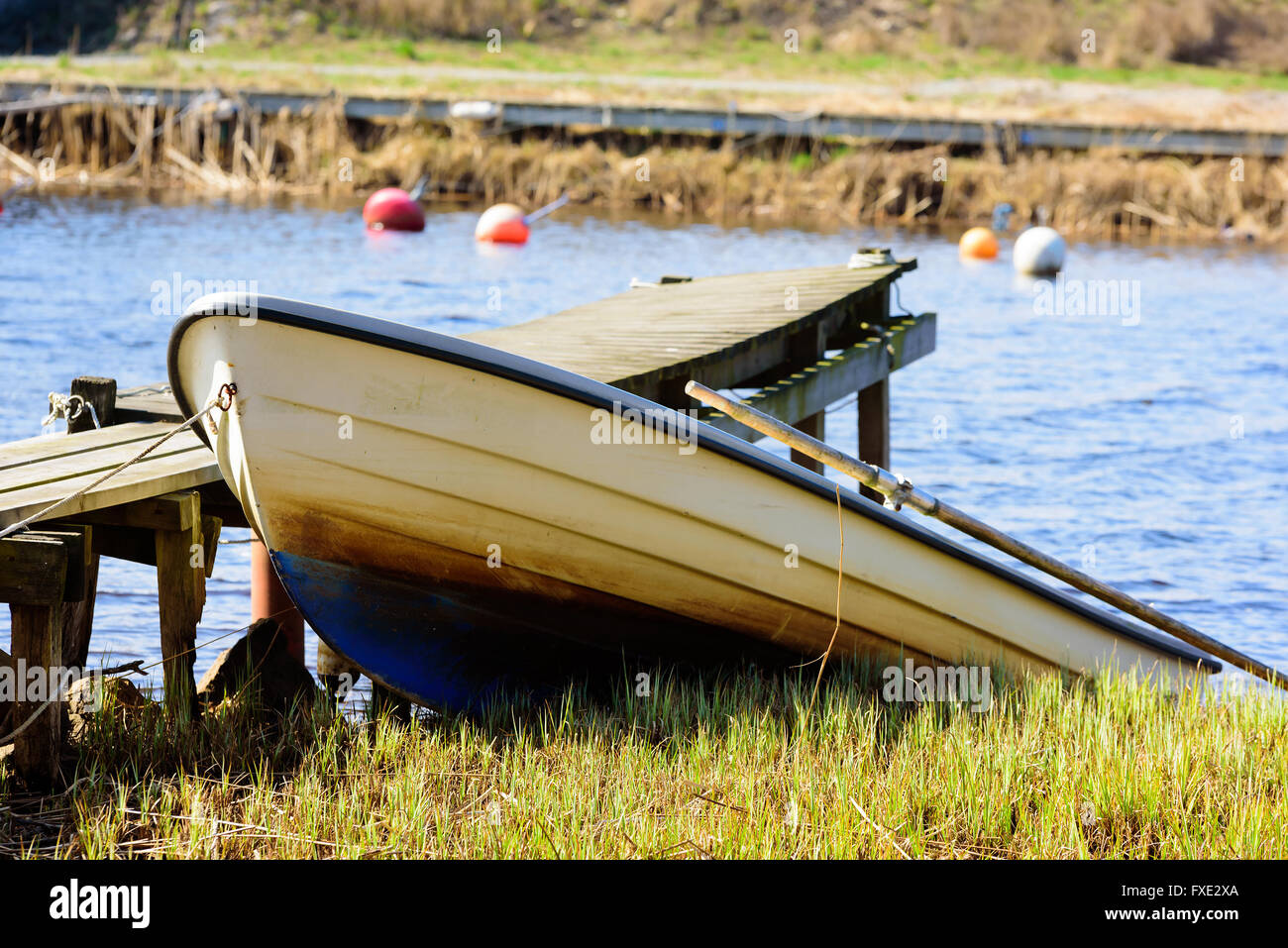 Small open rowboat pull up from the river beside a wooden pier. Stock Photo