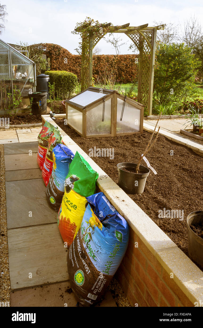 Bags of new compost stacked beside brick raised planter bed Stock Photo