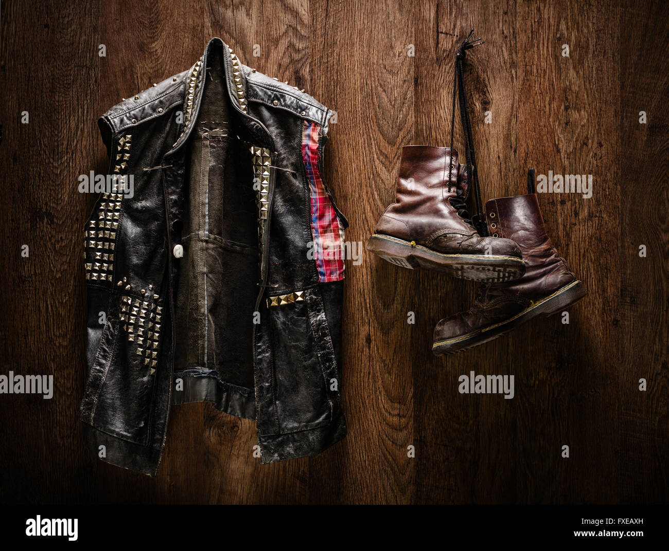 Punk-rock leather jacket and a pair of old boots hanging on a wooden wall Stock Photo
