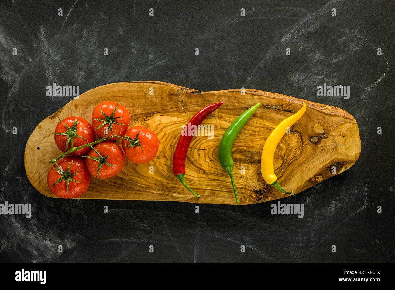 Tomatoes and hot chili peppers on wooden board. Stock Photo