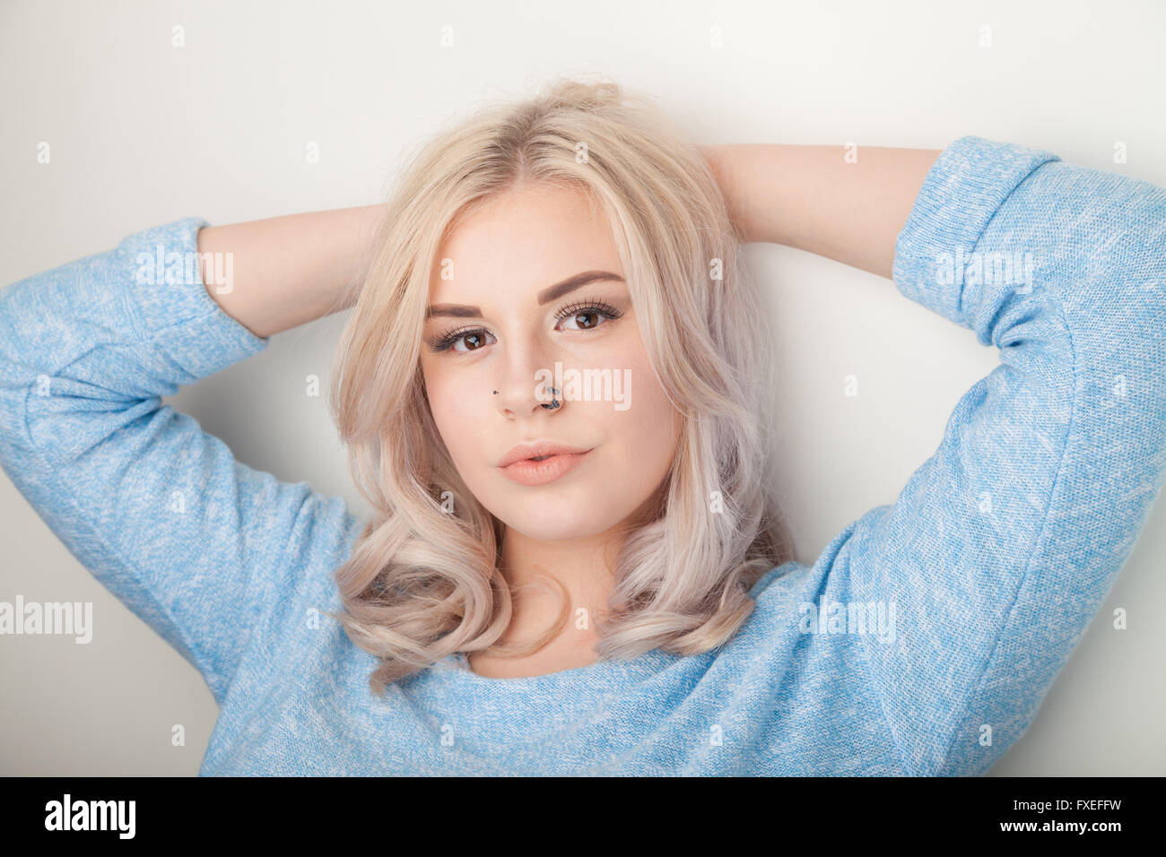 Blond teenage girl standing with arms behind her head. Stock Photo