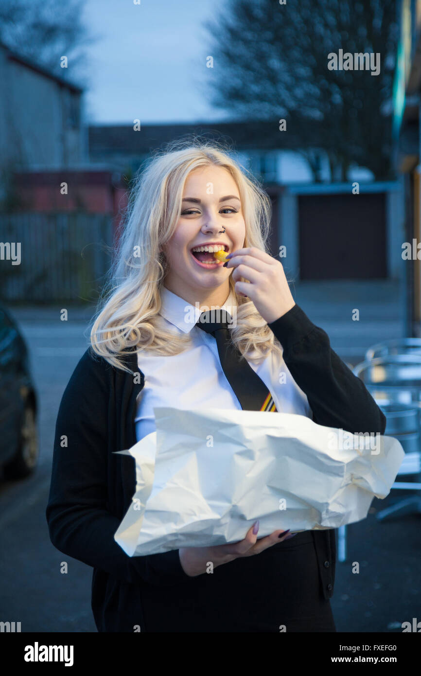 Blond schoolgirl eating takeaway chips outside. Stock Photo
