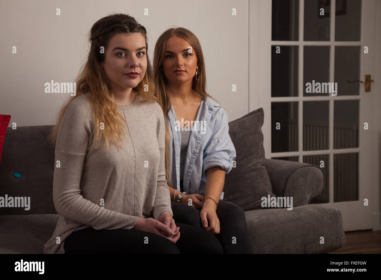 Two young women comforting each other at home on a sofa. Stock Photo