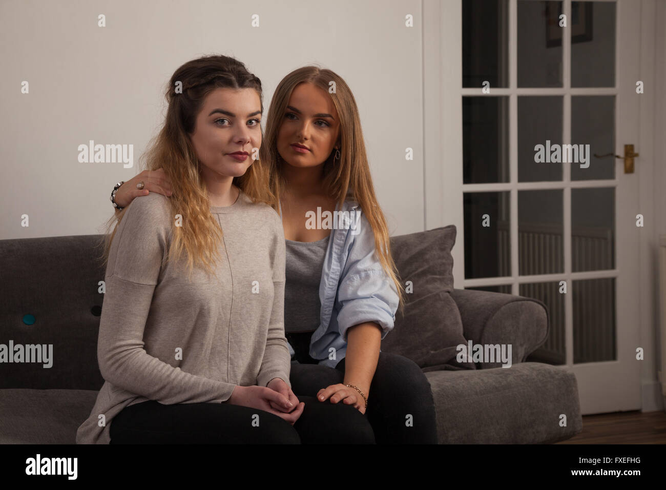 Two young women comforting each other at home on a sofa. Stock Photo