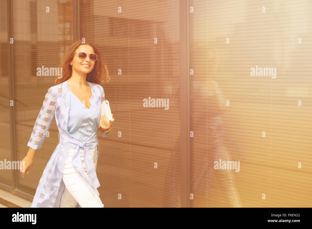 Young pretty businesswoman in sunglasses smiling and walking near business building. She is is a hurry to the meeting with her p Stock Photo