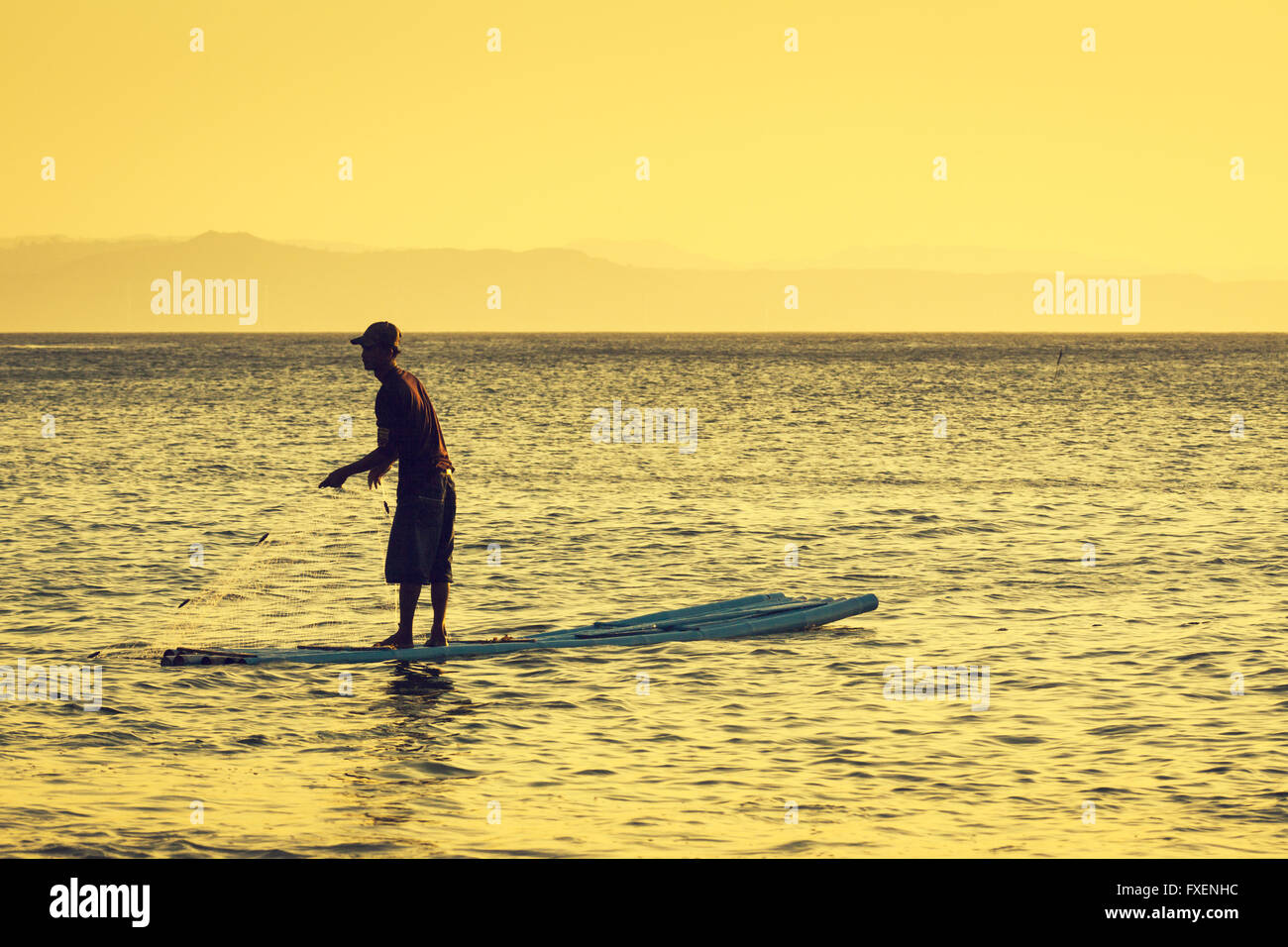 Filipino fishing the natural way from a simple bamboo raft with a backdrop of haze covered mountains at the end of the day Stock Photo