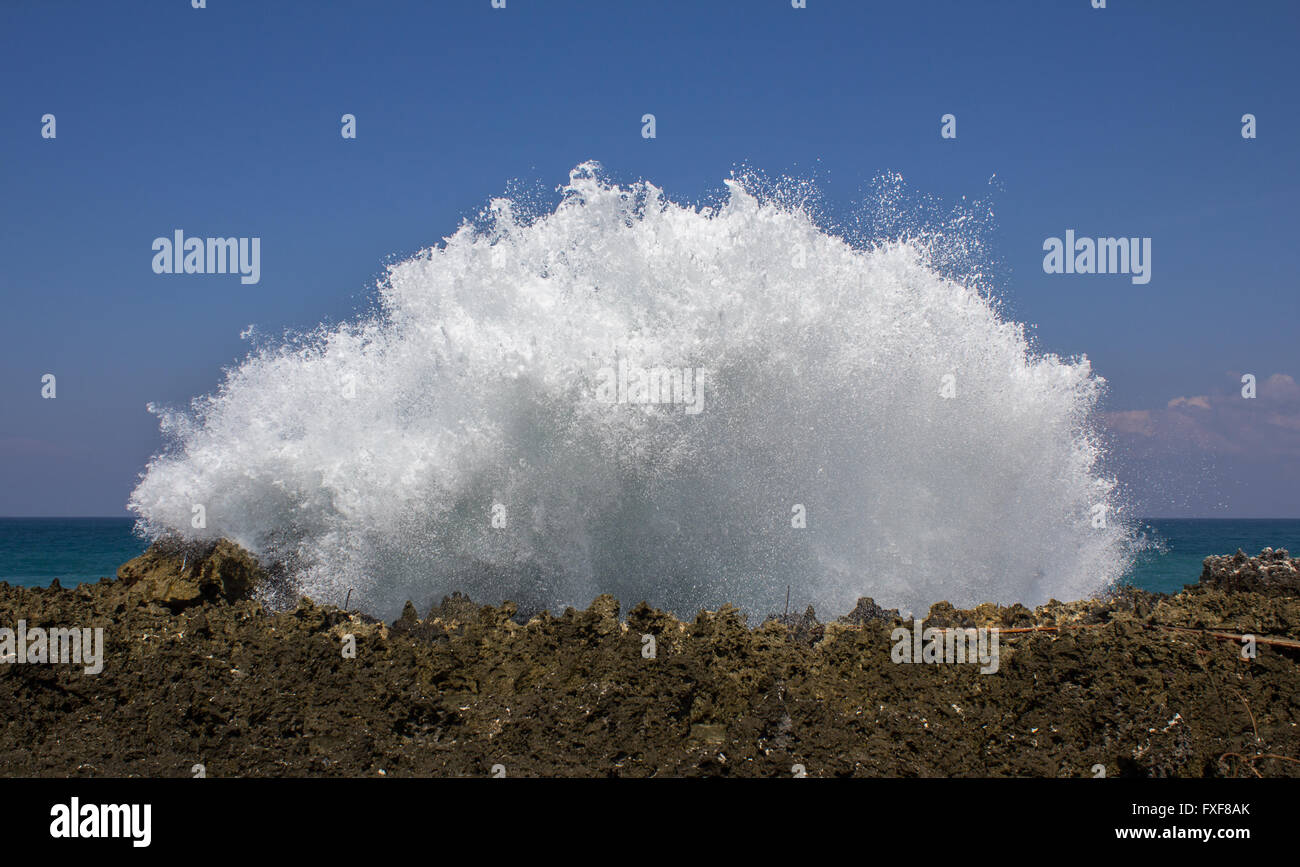 Huge Wave splashing against a rock wall creating white foam. Bali, Indonesia, Asia Stock Photo