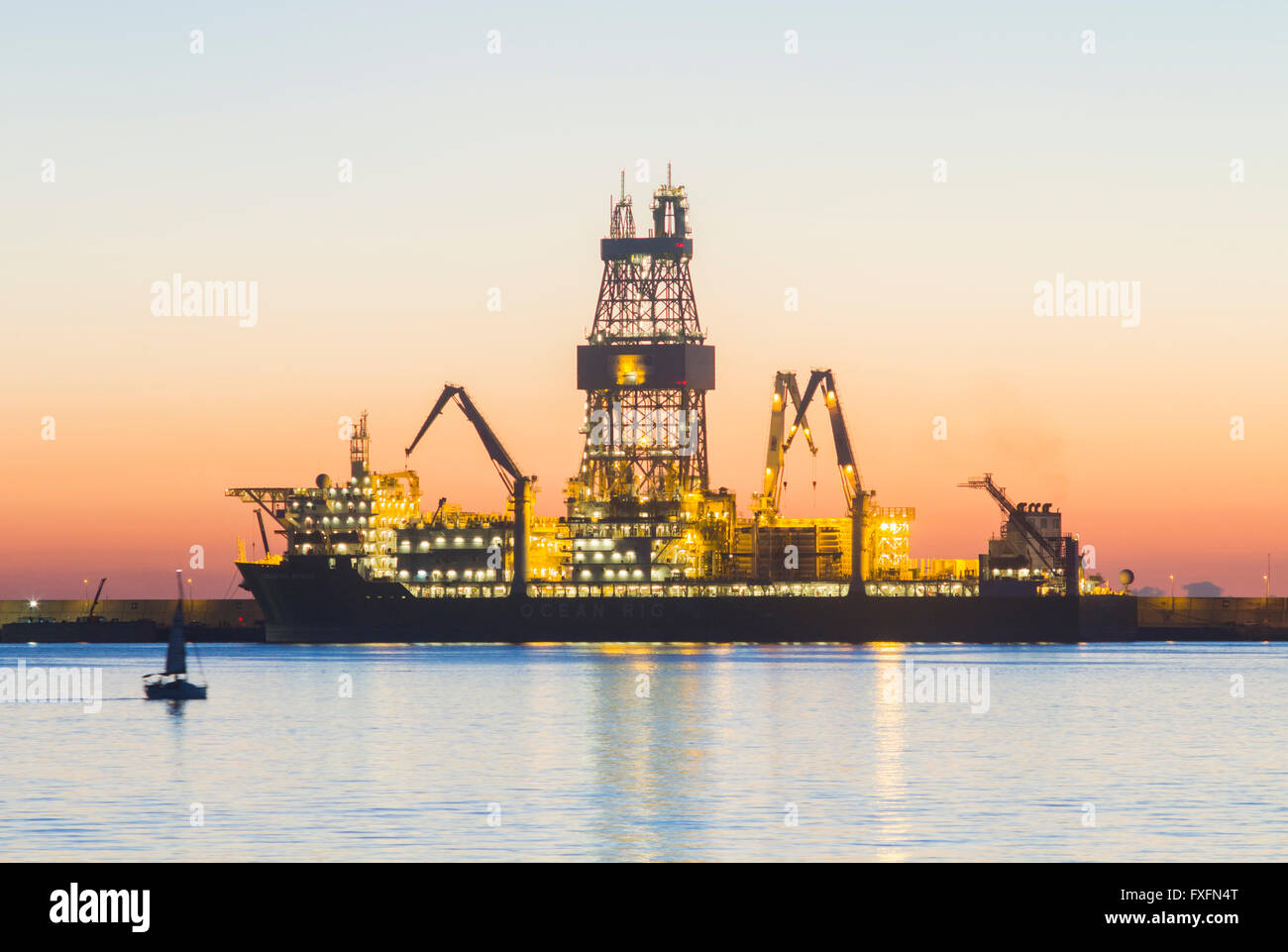 Las Palmas, Gran Canaria, Canary Islands, Spain, 15th April 2016. Weather: A yacht sails past an oil rig at sunrise in Las Palmas port on a glorious Thursday morning in Las Palmas, the capital of Gran Canaria. PICTURED: Las Palmas port is used by a number of oil companies for repairs, resupplying, and in the the case of some of the rigs/platforms in these images, for mothballing rigs for long periods due to the fall in oil prices and over supply of crude oil. Credit:  Alan Dawson News/Alamy Live News Stock Photo