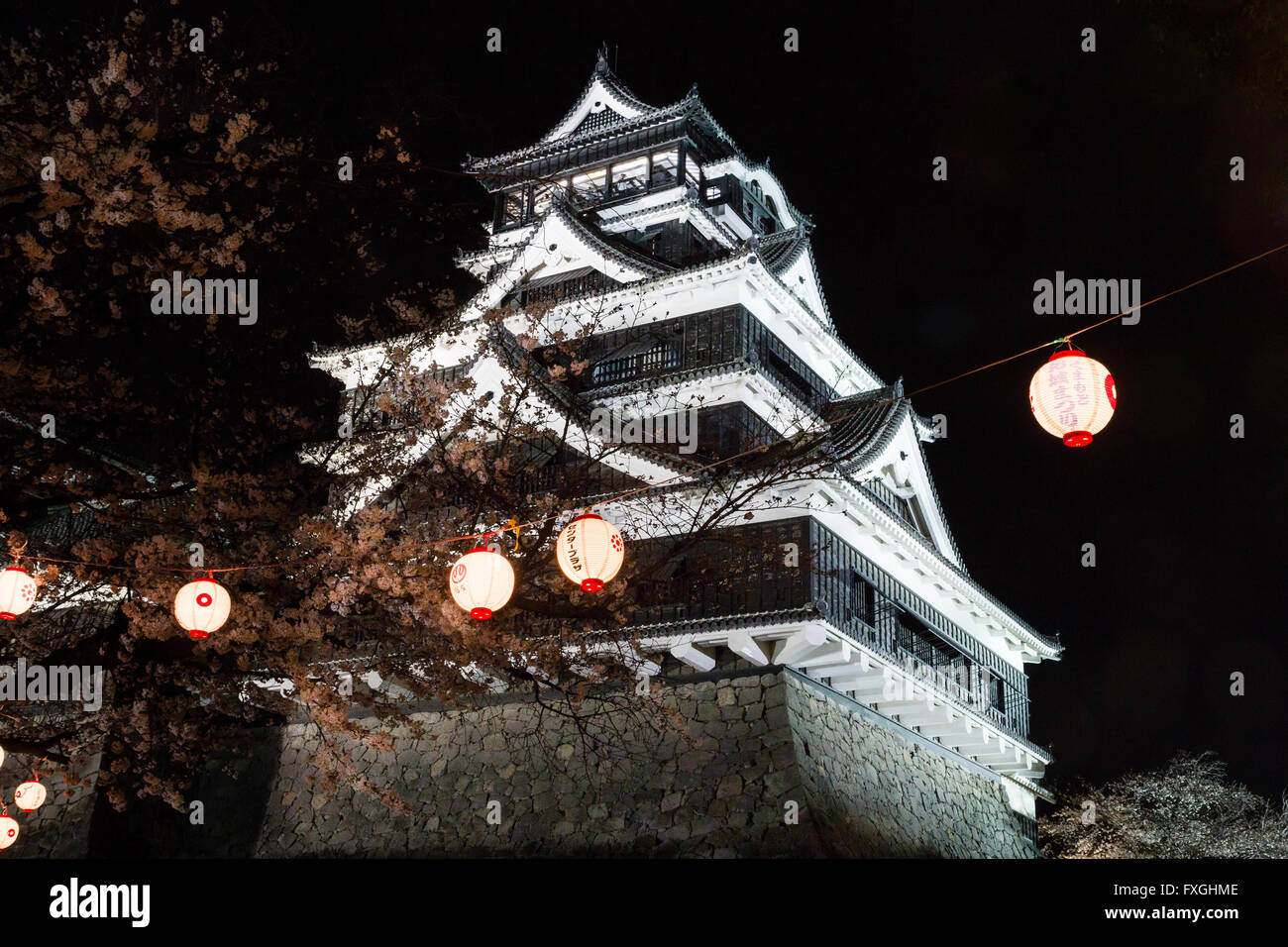 Kumamoto castle, the main keep, Daitenshu, illuminated at night during the spring time. Foreground, cherry blossoms and lanterns hanging Stock Photo