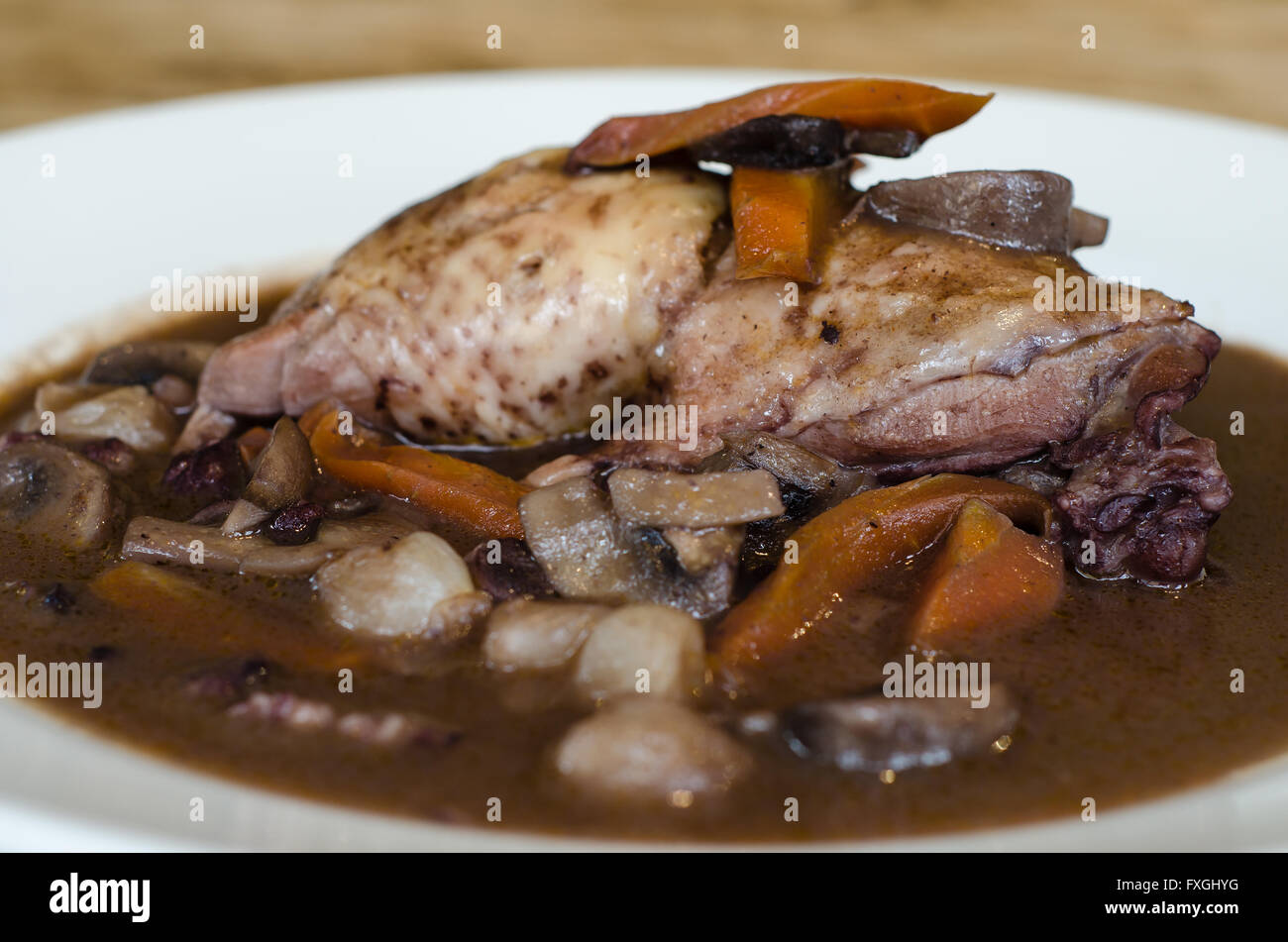Coq au vin natural light close from side. Classic French chicken dish prepared served with vegetables in red wine Stock Photo