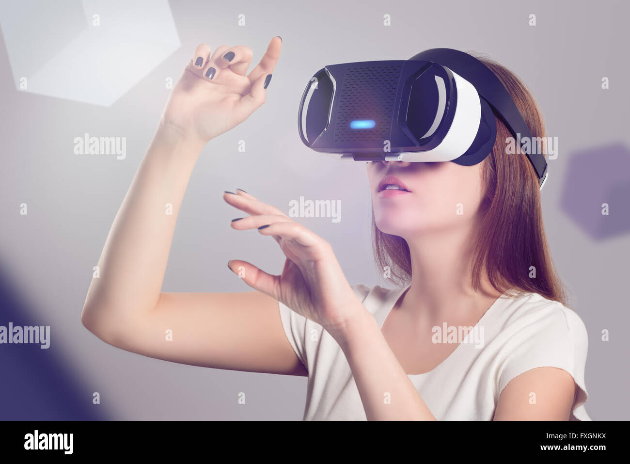 Woman in VR headset looking up and trying to touch objects in virtual reality. VR is a computer technology. Stock Photo