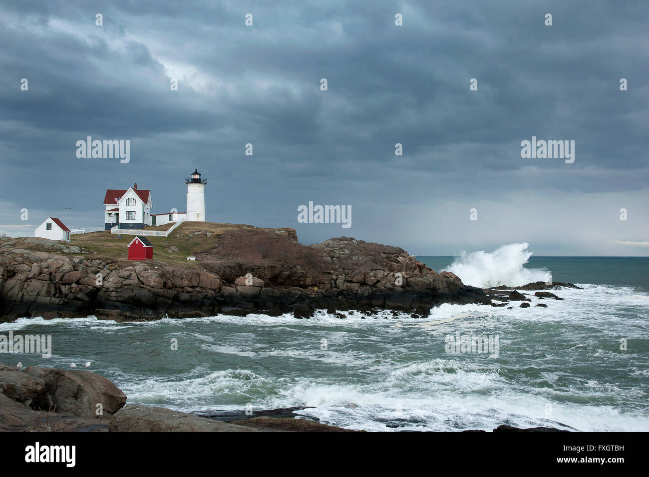 Storm clouds over Nubble lighthouse as waves crash on rocky coast of Maine. Stock Photo