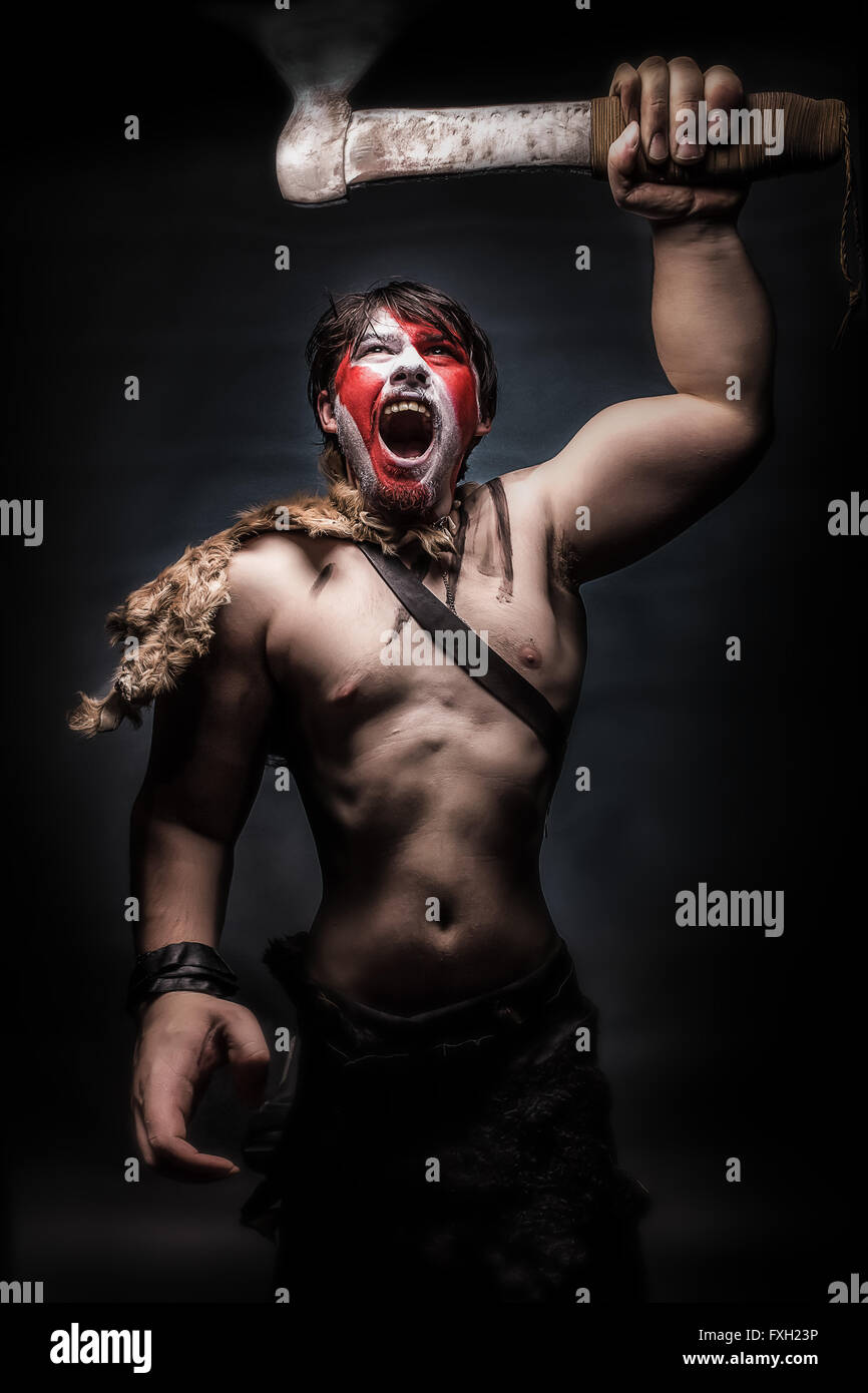 Painted image of man in war paint, with an ax in his hand, a warrior brandishing an ax furiously screaming, barbarian of ancient Stock Photo