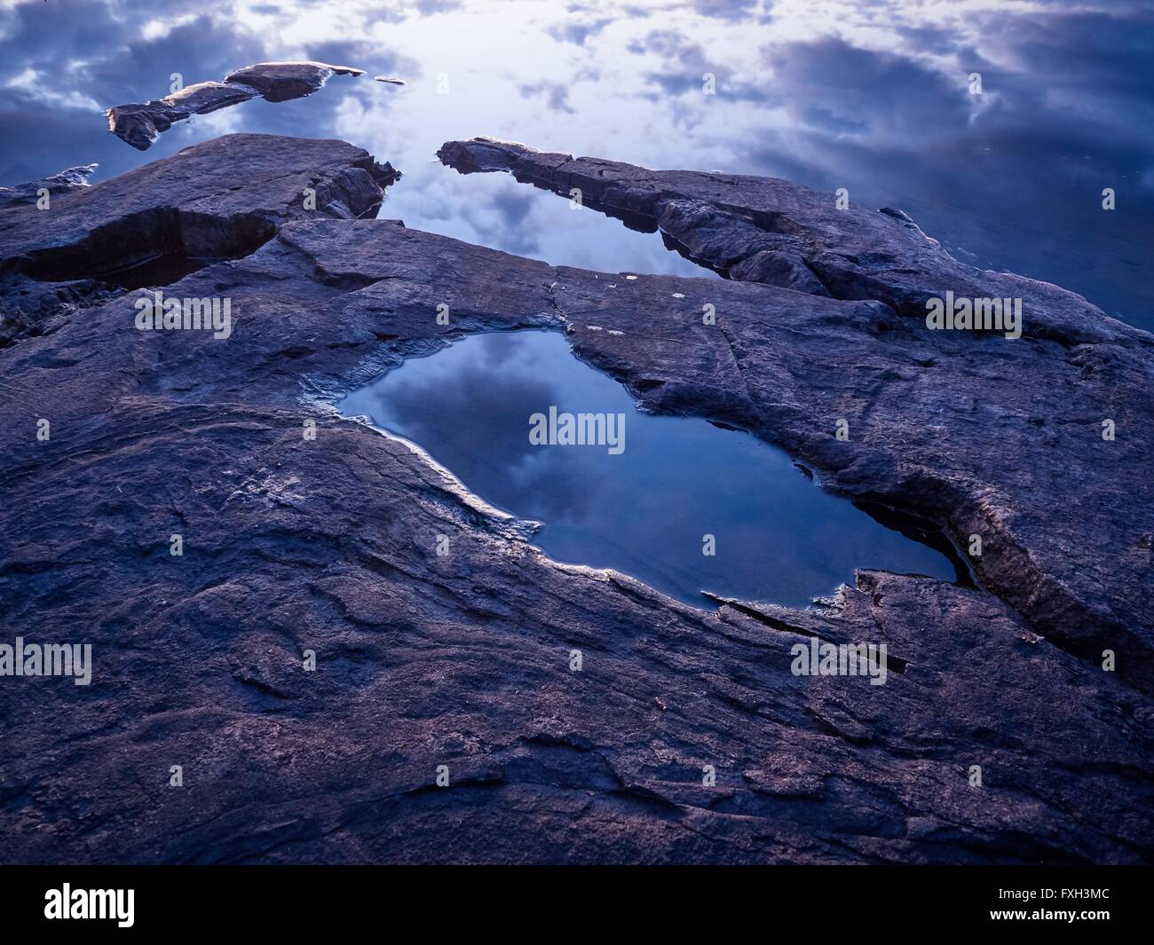 Reflection of cloudy blue sky between the rocks on the shore. Stock Photo