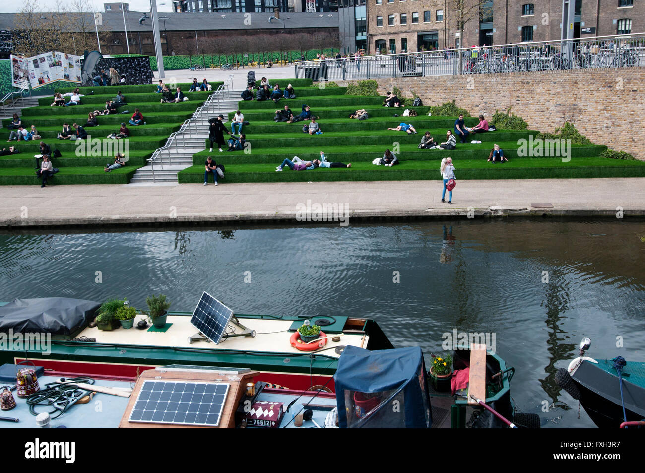 London. Kings Cross. Canal with Central St Martin's Art School in the background and people sat on bank terraces Stock Photo