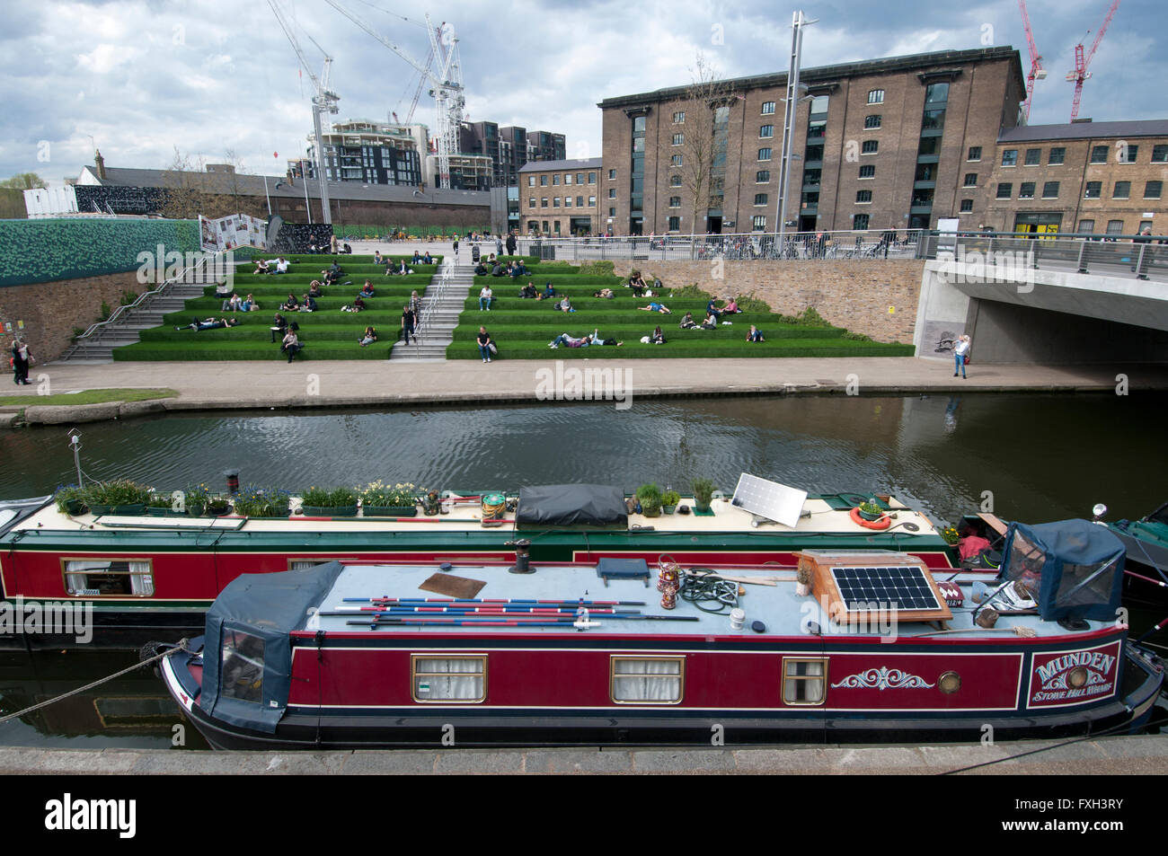 London. Kings Cross. Canal with Central St Martin's Art School in the background and people sat on bank terraces. Stock Photo