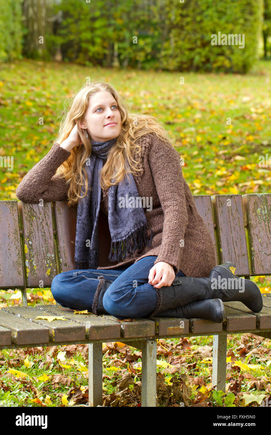 Young woman sitting on park bench in autumn Stock Photo - Alamy