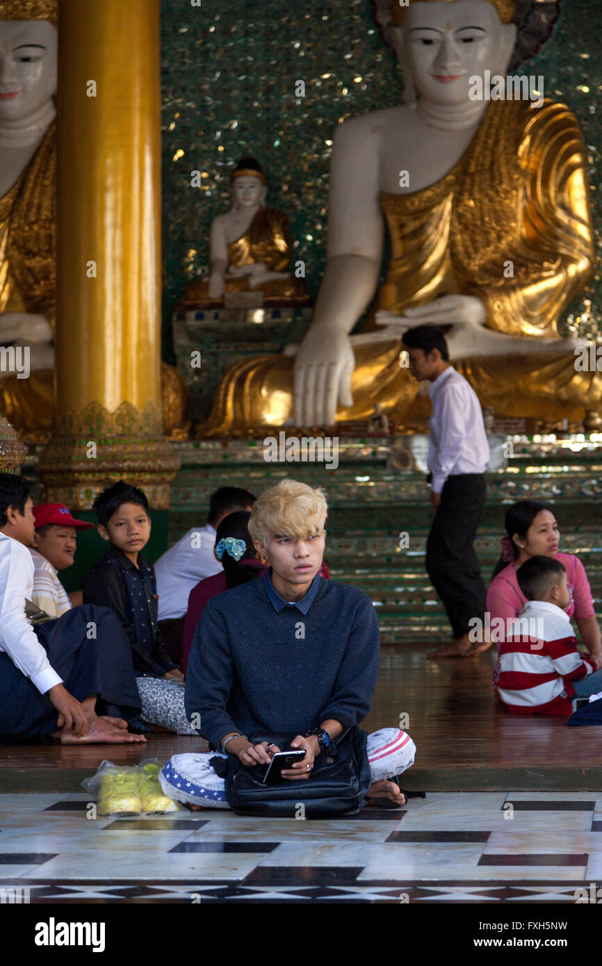 In an annex of the Paya Shwedagon, is this young cross-legged visitor whether a believer or a single portable phone user? Stock Photo
